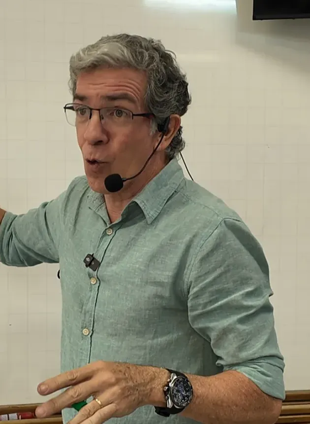 Professor Pinguim dando aula, de óculos e microfone