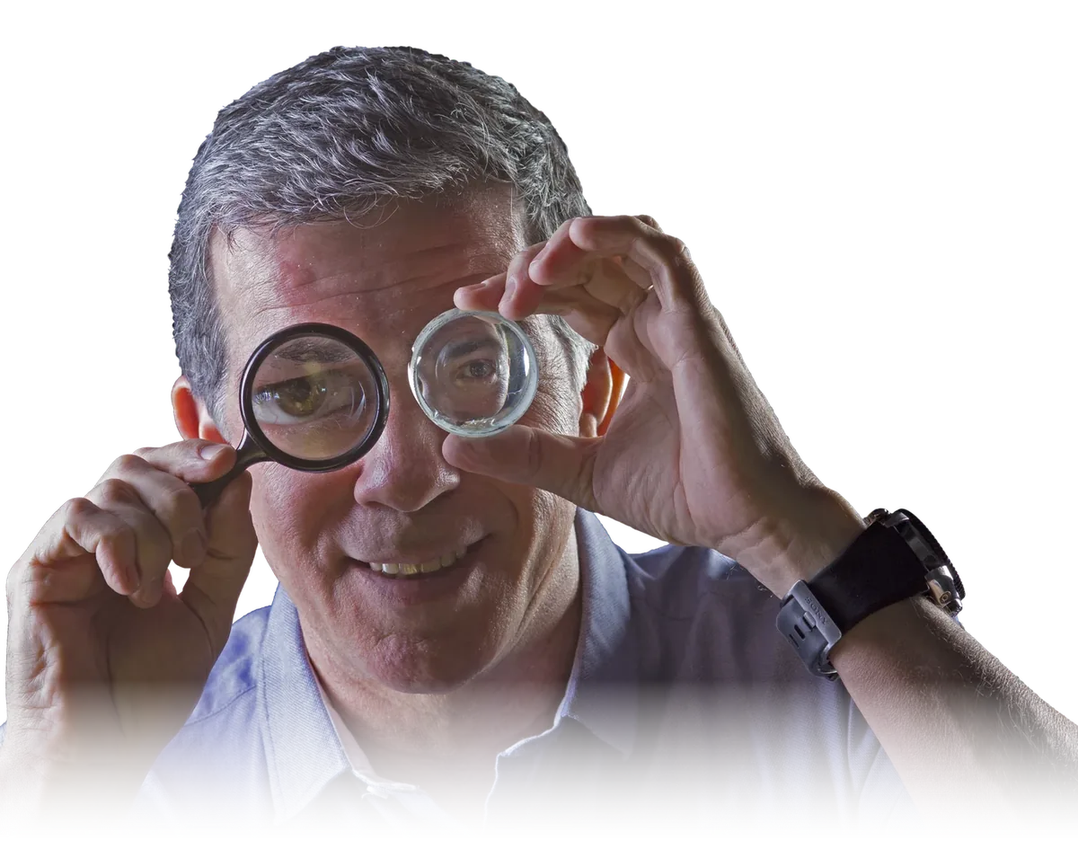 Professor Pinguim segurando uma lupa sobre o olho e olhando para a câmera